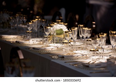 Elegant al fresco dining table set with gold cutlery and gilded glasses with moody shadows and sun-kissed atmosphere