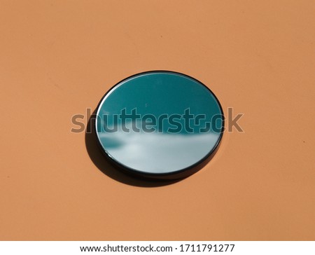 Elegant and artistic image of a mini circular mirror with reflections of the blue sky with clouds on a light and bright brown background
