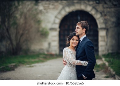 elegant asian bride hugging groom in castle yard - Powered by Shutterstock