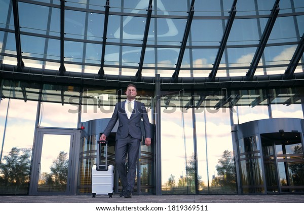 Elegant asian businessman checking email on mobile\
phone while walking with suitcase inside airport, experienced male\
employer using cell telephone while waiting for taxi car coming\
before work travel