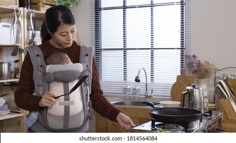 Elegant Asian Chinese Female Manager Carrying Baby Girl While Making Breakfast Meal At Modern Home Kitchen.