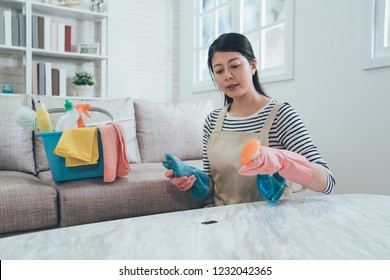 elegant asian housewife spray the cleaner on the dirt on table ready to remove it. wife in protective gloves wiping table with blue rag in living room with sunlight from window. woman doing housework - Shutterstock ID 1232042365