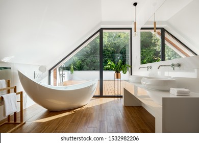 Elegant attic bathroom with stylish bathtub, wooden floor and balcony door