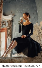 Elegant attractive female ballerina wearing black dress with long sleeves and smelling white rose in a rustic place. Powerful and expressive form. Copy space.