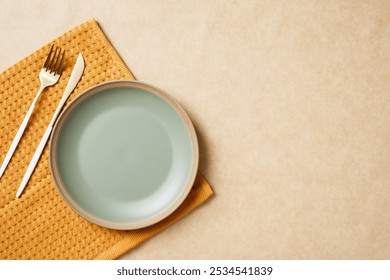 Elegant autumn table setting with a pastel green empty plate, gold cutlery, and yellow napkin on a textured beige background. Minimalist style. - Powered by Shutterstock