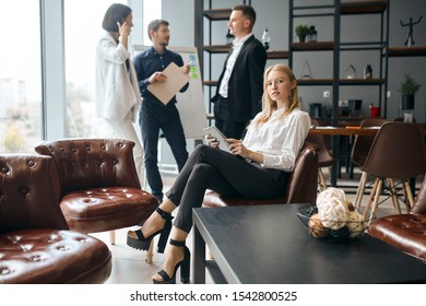 Elegant Awesome Female Boss Sitting With Laptop In Hands, Her Co-workers Havng A Conversation In The Background Of The Photo. Lifestyle, Job, Profession, Occupation