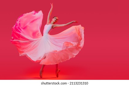 elegant ballerina in pointe shoes dancing in a long white skirt on red background