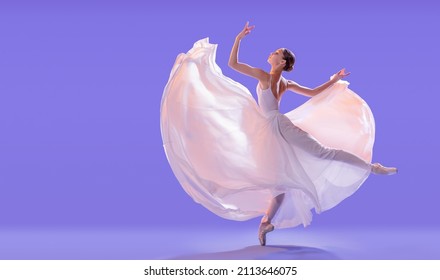 elegant ballerina in pointe shoes is dancing in a long flying white skirt on a lilac light background