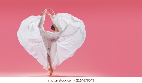 elegant ballerina in pointe shoes dancing in a long white skirt developing in the shape of a heart on a pink background
