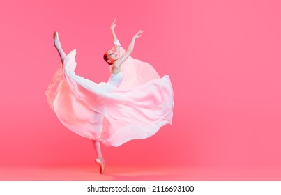 elegant ballerina in pointe shoes dancing in a long white skirt on pink background
