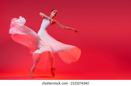 elegant ballerina in pointe shoes dancing in a long white skirt on red background