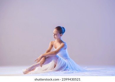 elegant ballerina in pointe shoes sits with her legs stretched out in a long white skirt on white background - Powered by Shutterstock