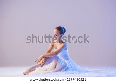 elegant ballerina in pointe shoes sits with her legs stretched out in a long white skirt on white background
