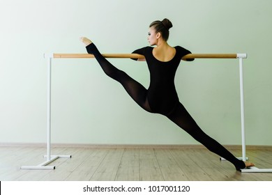 Elegant beautiful ballerina with a perfect body doing stretching twine exercise with barre in dance ballet studio. dancer girl barres. Sexy brunette trains. Dark tights. lifted one leg.