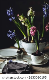 Elegant beautiful dinner table setting with a floral composition with bulbous hyacinth flowers as centrepiece. Easter celebration. White wine, vintage tableware. Bohemian style. Dark background