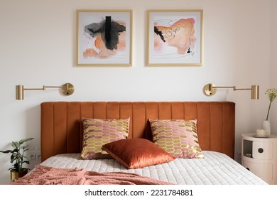 Elegant bedroom with art, golden lamps and stylish bed with velvet, ocher colored headboard