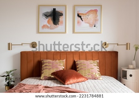 Elegant bedroom with art, golden lamps and stylish bed with velvet, ocher colored headboard