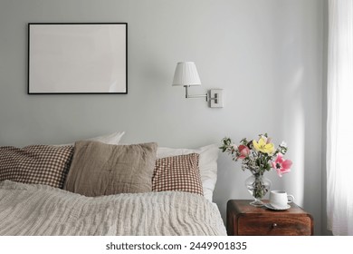 Elegant bedroom. Tulips, cherry tree blossoms bouquet in glass vase. Wooden night stand. Cup of coffee. Blank black picture frame mockup. Lamp, pleated shade on mint wall, checkered pillows. - Powered by Shutterstock