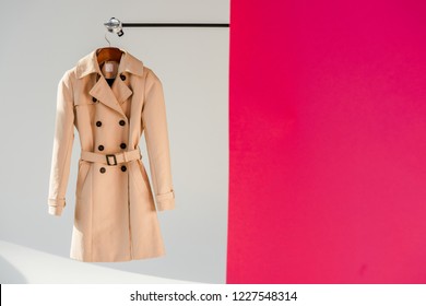 elegant beige trench coat on hanger at pink and grey background 