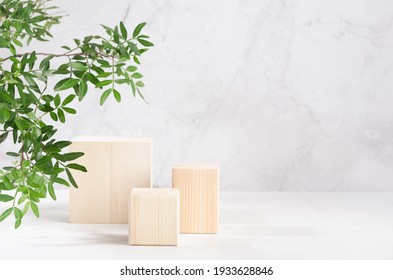 Podiums élégants cubiques en bois beige avec feuillage vert luxuriant au soleil sur une planche blanche et mur en marbre gris pour l'affichage du produit. Un design d'été simple et moderne.