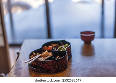 Elegant bento box with intricate patterns, containing assorted food, accompanied by chopsticks, set on a wooden table with a cup nearby. - Powered by Shutterstock