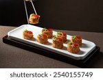 Elegant bite-sized appetizers arranged on rectangular white platter; garnished with vibrant red and green toppings.