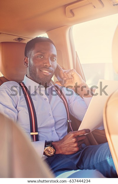 Elegant black American male read the paper\
document in a car. Filtered warm toned\
image.
