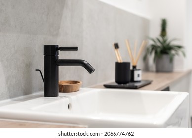 An elegant black bathroom faucet and white square sink with a blurry cup, toothbrushes and plant - Shutterstock ID 2066774762