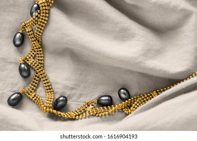 Elegant black pearl gold necklace on beige draped linen closeup
