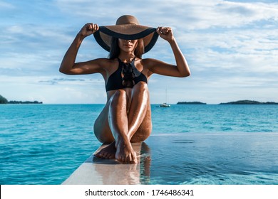Elegant black swimsuit swimwear model woman with contrast brim sun hat on infinity pool luxury resort vacation. High end fashion for wellness spa , hair removal laser legs and body pedicure skincare.