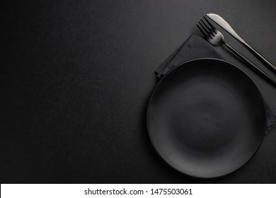 Elegant black table setting: plates, napkin and silverware over black background. Flat lay. copy space