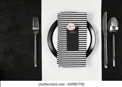 Elegant black and white table setting: plates on linen, striped napkin, blank label with rose and silverware. Top view point. - Powered by Shutterstock