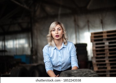 Elegant Blonde Woman Pushing A Big Truck Tire In An Abandoned Wear House