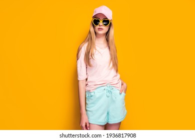 Elegant blonde woman wearing fashion cap, sunglasses enjoying sun on yellow summer background