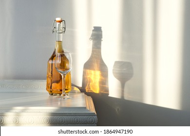 Elegant bottle with alcohol and empty glass over a vintage cabinet and a beautiful sun reflection on the wall - art concept