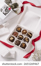 An elegant box of assorted chocolates featuring various toppings artfully arranged. The sophisticated packaging is complemented by a ribbon, perfect for gifting at a celebration.