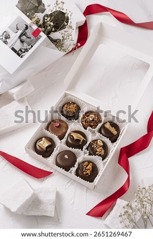 An elegant box of assorted chocolates featuring various toppings artfully arranged. The sophisticated packaging is complemented by a ribbon, perfect for gifting at a celebration.
