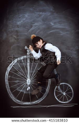 Elegant boy in a suit, bowler hat and glasses posing by a painted retro bicycle. Old Europe style, England. Little gentleman. Kid's fashion.