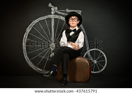 Elegant boy in a suit, bowler hat and glasses stands by a painted retro bicycle. Old Europe style, England. Little gentleman. Kid's fashion.