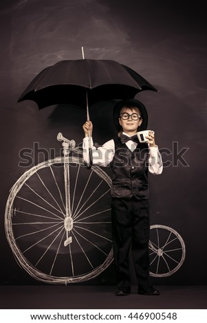 Elegant boy in a suit, bowler hat and glasses stands by a painted retro bicycle. Old Europe style, England. Little gentleman. Kid's fashion.