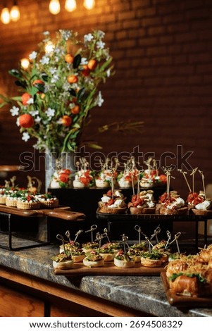 Elegant buffet table featuring mini sandwiches, pastries, canapes and fresh blooms against a moody black background.