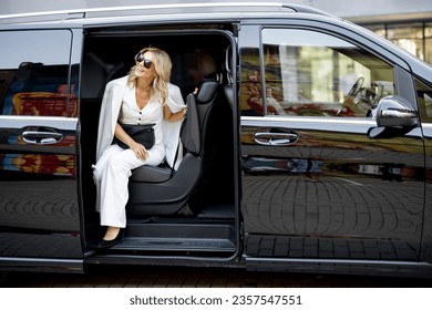 Elegant business lady in white looks out of a minivan taxi. Concept of business trips and transportation - Shutterstock ID 2357547551