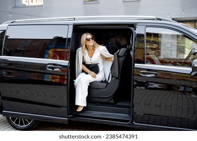 Elegant business lady in white looks out of a minivan taxi. Concept of business trips and transportation