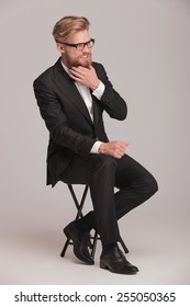 Elegant Business Man Sitting On A Stool, Smiling Away From The Camera While Fixing His Beard.