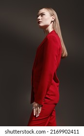 Elegant business style. Portrait of a beautiful young woman with elegant makeup posing in smart red pantsuit on a dark background. Femininity, feminism and fashion.