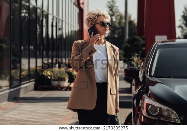 Elegant Business Woman with Briefcase in Hand\
Talking on Phone Near the Luxury\
Car