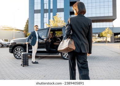 Elegant business woman walks to the luxury car, man with a suitcase opens vehicle door, letting lady in. Concept of business trip and travel - Powered by Shutterstock