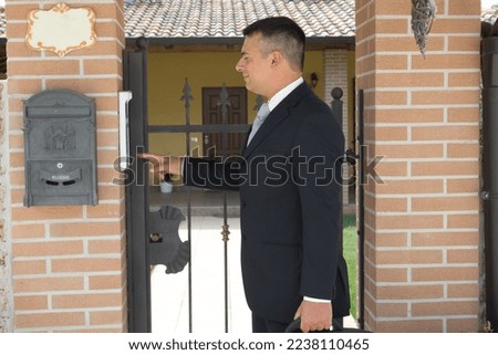 Elegant businessman with briefcase ringing the intercom of a house. Scammer and persistent salesman on the hunt for victims

