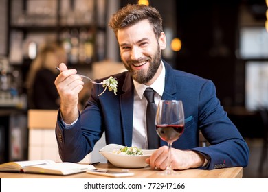 Elegant businessman dressed in the suit having a dinner with salad and wine sitting at the modern restaurant interior - Powered by Shutterstock