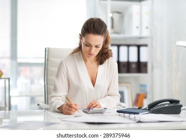 An Elegant Businesswoman Is Concentrating While Sitting At Her Desk In A Modern Office, Crunching Numbers.